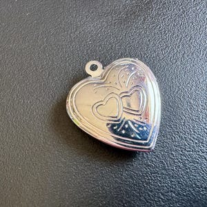 Peut inclure: Un médaillon en argent en forme de cœur avec un motif détaillé de deux cœurs entrelacés.