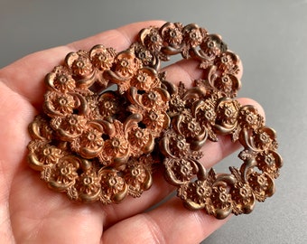 Könnte beinhalten: Drei antike Messingfiligranverzierungen mit floralem Design. Die Verzierungen sind kreisförmig und haben eine erhabene, strukturierte Oberfläche.