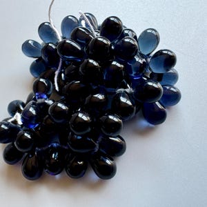 May include: A cluster of dark blue glass beads in a teardrop shape. The beads are strung together with a white thread.