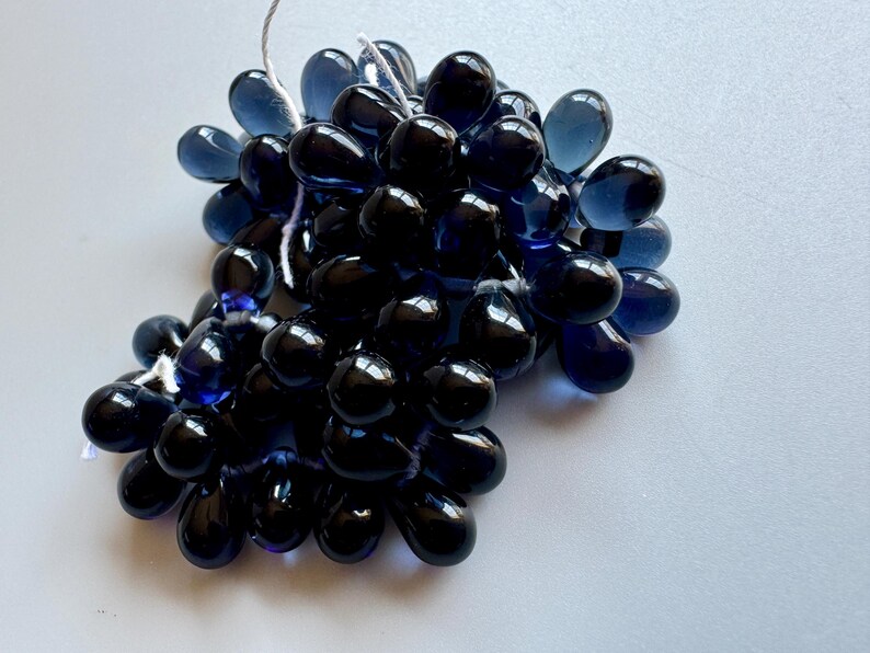May include: A cluster of dark blue glass beads in a teardrop shape. The beads are strung together with a white thread.