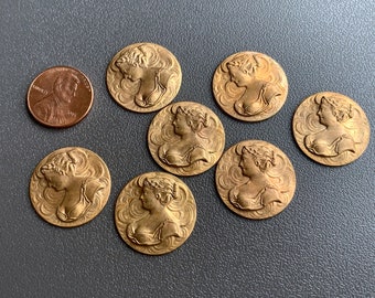 May include: Seven gold-toned metal buttons with a raised design of a woman's profile. The buttons are circular and have a slightly textured surface.