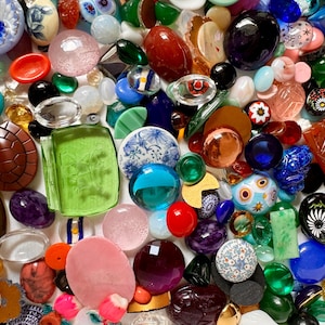 May include: A collection of colorful glass and ceramic buttons, beads, and other decorative elements. The assortment includes various shapes, sizes, and patterns, with a mix of opaque and translucent materials.