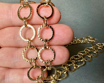 May include: A gold chain necklace with textured, circular links. The chain is made of multiple rows of linked circles.