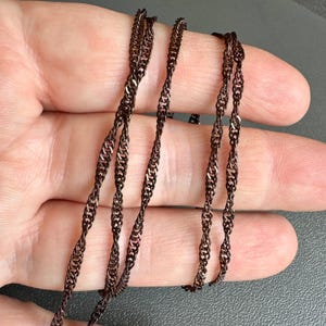Könnte beinhalten: Nahaufnahme einer braunen Kettenkette mit einem gedrehten Design. Die Kette ist aus Metall und hat eine glänzende Oberfläche.