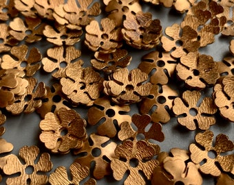 Puede incluir: Primer plano de un montón de adornos metálicos en forma de flor de color dorado. Los adornos tienen una superficie texturizada y un agujero en el centro.