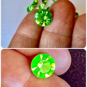 May include: Close-up of several round, faceted, bright green gemstones. One gemstone is held between fingers, with others scattered in the background. The gems have a brilliant, reflective quality, showcasing their cut and colour.