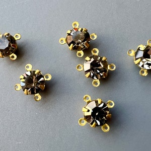 May include: Six gold-toned metal settings with clear, faceted, round rhinestones. Each setting has four loops for attaching to a jewelry piece.