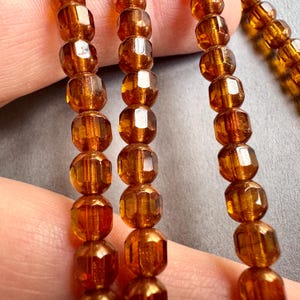 May include: A strand of amber glass beads with a faceted finish. The beads are round and have a shiny, translucent appearance.