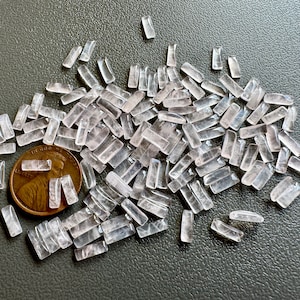 May include: A pile of small, clear, rectangular, rose quartz crystals. The crystals are about the size of a ten pence coin.
