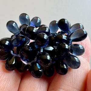 May include: A cluster of dark blue glass beads in a teardrop shape. The beads are strung together and have a glossy finish.
