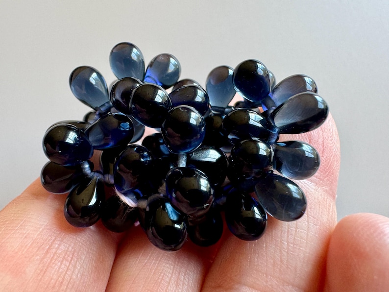 May include: A cluster of dark blue glass beads in a teardrop shape. The beads are strung together and have a glossy finish.