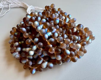 May include: A strand of iridescent brown teardrop-shaped glass beads. The beads have a pearlescent finish and are strung on a white thread.