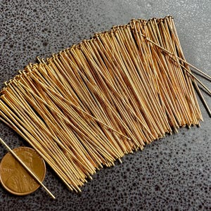 May include: A large quantity of gold-colored head pins, arranged in a fan shape. A US penny is included for scale.