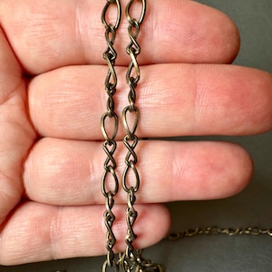 May include: Close-up of a gold-toned chain with a twisted, interwoven design. The chain is made of small, oval-shaped links.