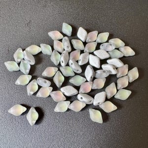 以下が含まれることがあります： 白、グレー、虹色のパステルカラーのフロスト加工されたひし形ビーズのコレクション。各ビーズには、糸を通すための穴があります。ビーズは濃い灰色の表面に散らばっており、ジュエリー作りに適しています。