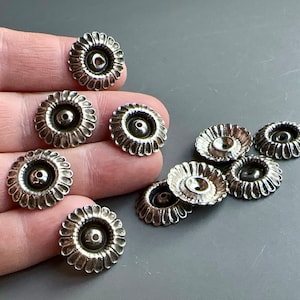 May include: A collection of silver-toned metal flower-shaped embellishments with a hole in the center. The embellishments are arranged on a hand.