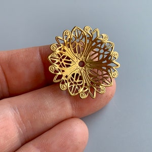 Puede incluir: Adorno de metal dorado filigranado con forma circular y un intrincado diseño floral. El adorno tiene un pequeño agujero en el centro.