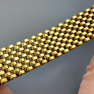 May include: A gold-colored metal bracelet with a woven chain link design.
