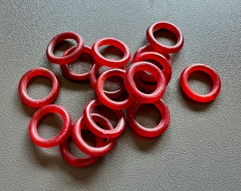 May include: A collection of translucent red O-rings scattered on a grey surface. The rings are circular with a hole in the centre. The lighting highlights the texture and colour of the rings.