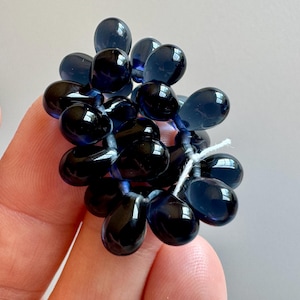 May include: A cluster of dark blue glass beads in the shape of teardrops, strung together on a white thread.