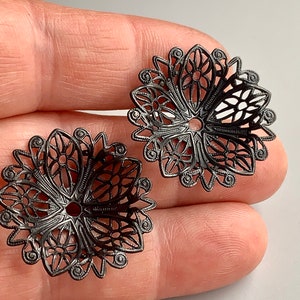 Puede incluir: Dos adornos de metal negro filigranado con un diseño floral. Los adornos son redondos y tienen un agujero en el centro.