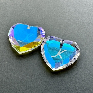 May include: Two iridescent heart-shaped crystal charms with a clear blue centre and a white letter "X" etched inside.