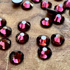 Puede incluir: Una dispersión de pequeños diamantes de imitación facetados de color morado oscuro sobre una superficie de madera.