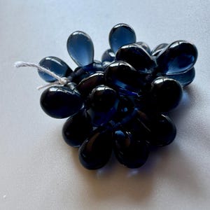 May include: A cluster of dark blue glass teardrop beads, strung together with white thread.