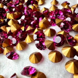 May include: A close-up of a pile of pink and gold rhinestones. The rhinestones are scattered on a white surface.
