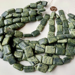 May include: Strung beads in shades of green and dark gray. The beads are rectangular with rounded edges and a mottled, textured appearance. The beads are strung together on a white string, ready for jewelry making.