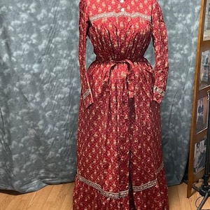 May include: A long-sleeved red dress with a floral print and white trim. The dress has a high neckline and a button-up front.