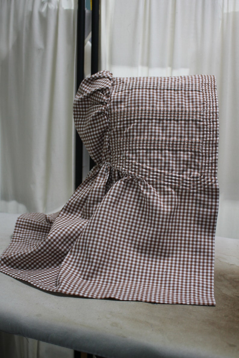 May include: A brown and white gingham bonnet with a gathered ruffle at the crown.
