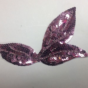 Könnte beinhalten: Eine rosa paillettenbesetzte Blattapplikation mit einem zarten Design. Diese Verzierung ist perfekt, um Kleidung, Accessoires oder Bastelarbeiten mit einem Hauch von Glanz zu versehen.