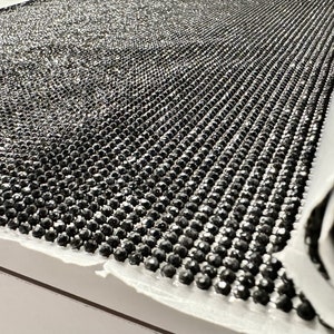 May include: A roll of black rhinestone trim with a shiny, reflective finish. The trim is made of small, round rhinestones that are closely spaced together.