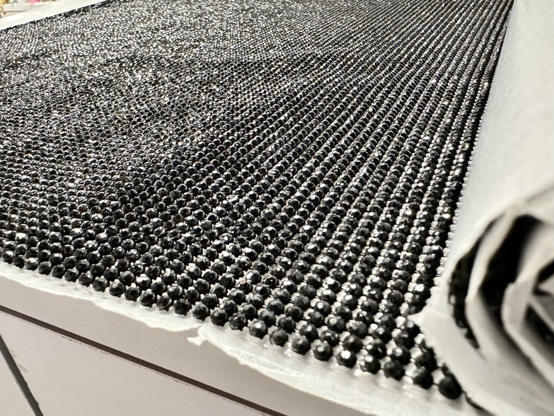 May include: A roll of black rhinestone trim with a shiny, reflective finish. The trim is made of small, round rhinestones that are closely spaced together.