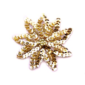 May include: Gold sequin flower applique. The flower is made of small, round sequins that are sewn together in a circular pattern. The sequins are arranged in a way that creates a starburst effect.