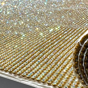 May include: A roll of gold mesh fabric with clear iridescent rhinestones. The fabric is rolled up and the rhinestones are visible on the surface.