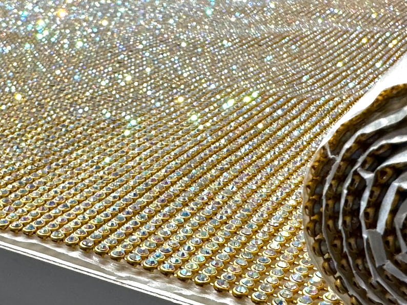May include: A roll of gold mesh fabric with clear iridescent rhinestones. The fabric is rolled up and the rhinestones are visible on the surface.