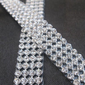 May include: A close-up of a silver rhinestone trim with multiple rows of clear rhinestones.