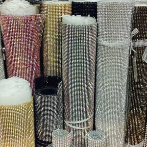 May include: Rolls of iridescent rhinestone trim in various colors, including silver, gold, black, and pink. The trim is made of small, sparkling rhinestones.