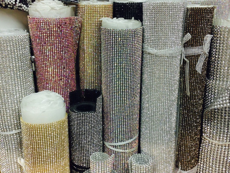 May include: Rolls of iridescent rhinestone trim in various colors, including silver, gold, black, and pink. The trim is made of small, sparkling rhinestones.