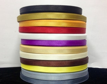 May include: A stack of 14 different colored ribbon spools. The colors are black, gold, yellow, red, white, purple, beige, ivory, brown, yellow, gray, and black.