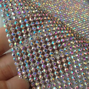 May include: A sheet of iridescent rhinestones on a silver mesh backing. The rhinestones are small and closely spaced, creating a shimmering effect.