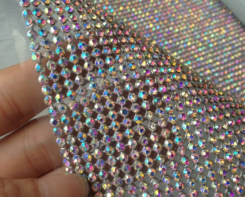 May include: A sheet of iridescent rhinestones on a silver mesh backing. The rhinestones are small and closely spaced, creating a shimmering effect.
