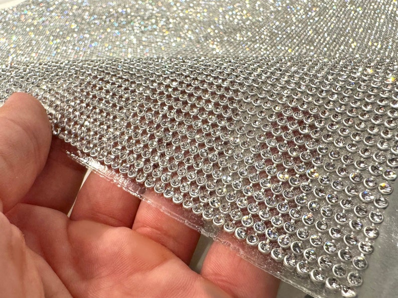 May include: A sheet of clear adhesive-backed rhinestones, arranged in a grid pattern. The rhinestones are small and round, with a clear, iridescent finish.