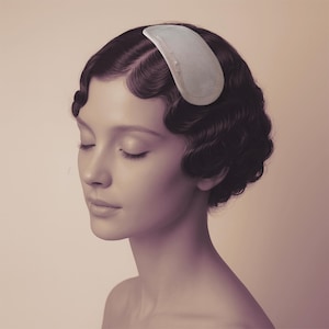 May include: A sepia-toned portrait of a person with dark, wavy hair styled in the vintage finger wave technique. A light-coloured hair accessory is pinned to the side. The person's eyes are closed, and the overall aesthetic is soft and elegant.