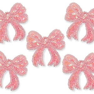 May include: Five pink sequined bows are displayed against a white backdrop. Each bow is adorned with sequins, giving a shimmering appearance. The bows are a delicate pink, suitable for decorating crafts or accessories.