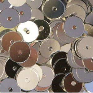 May include: A pile of silver round sequins with a hole in the centre. The sequins are shiny and reflective.