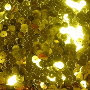 Può includere: Un'immagine ravvicinata di un mucchio di paillettes dorate luccicanti. Le paillettes sono rotonde e hanno un foro al centro. Sono perfette per l'artigianato e la decorazione.