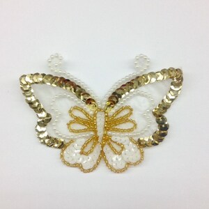 May include: A white and gold butterfly-shaped applique with sequins and beads.